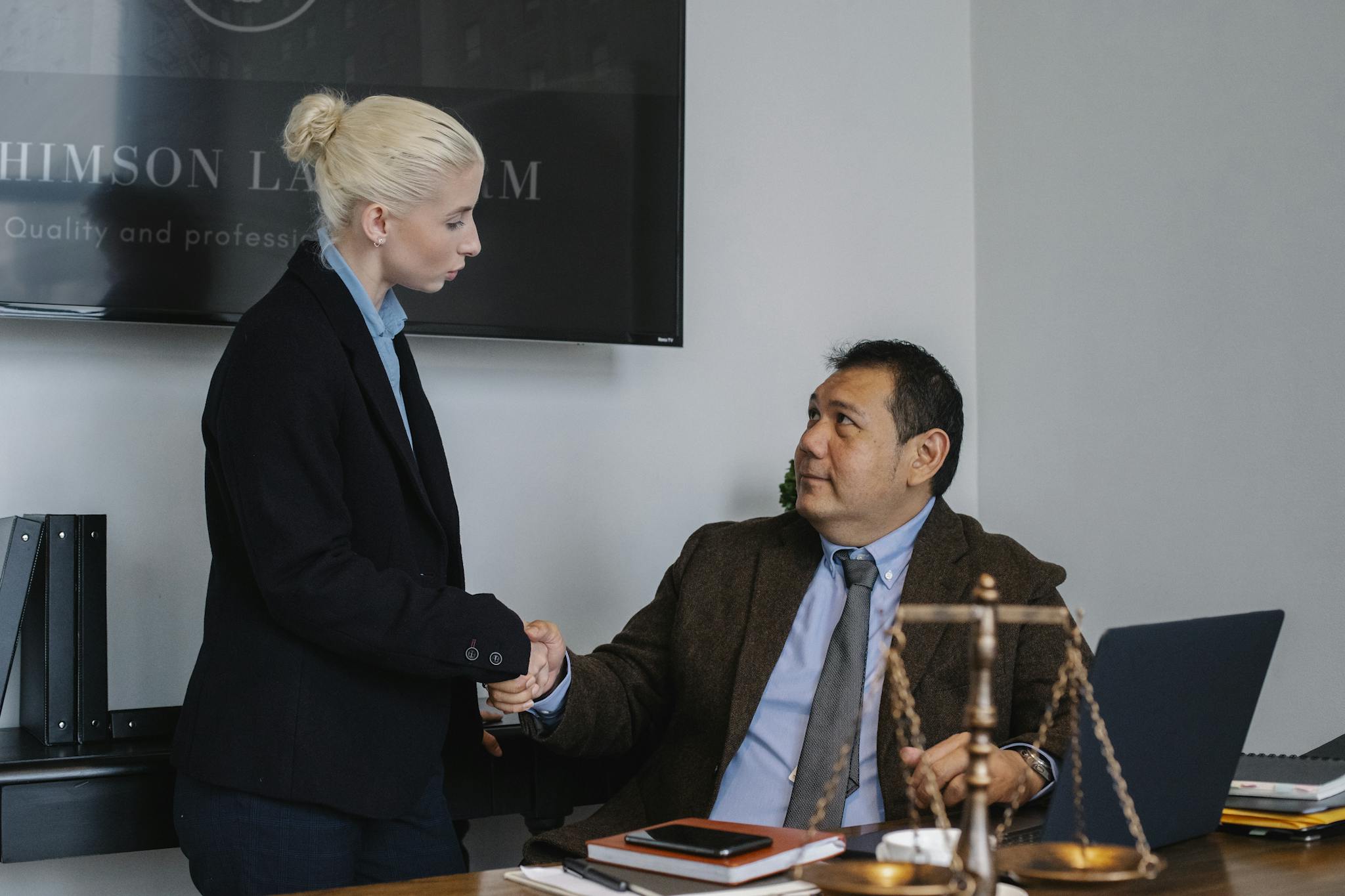 A male and female professional shaking hands in a law office environment.